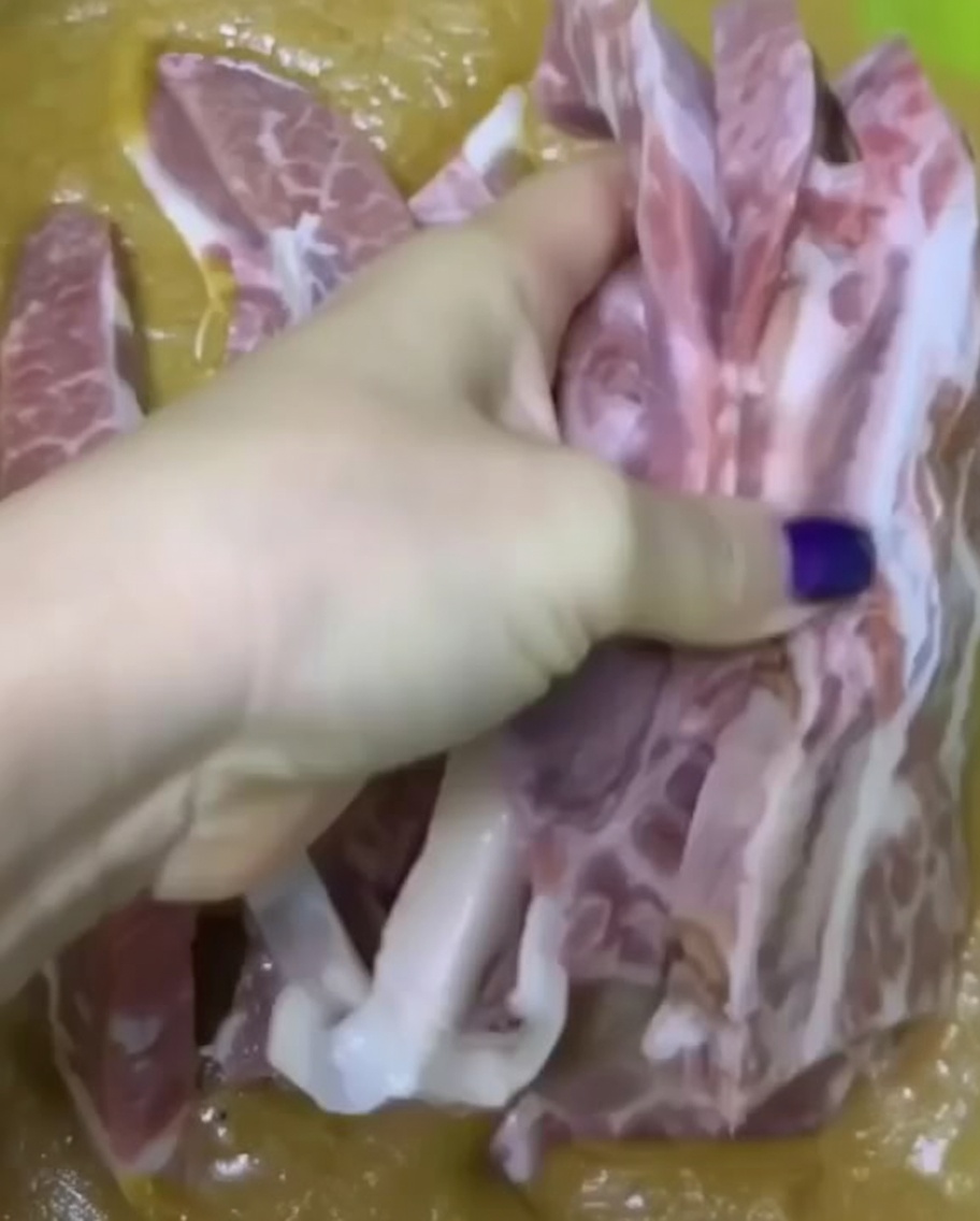 Une main trempant des morceaux de côtelettes de bœuf crues dans une marinade épaisse et mixée dans un bol vert.