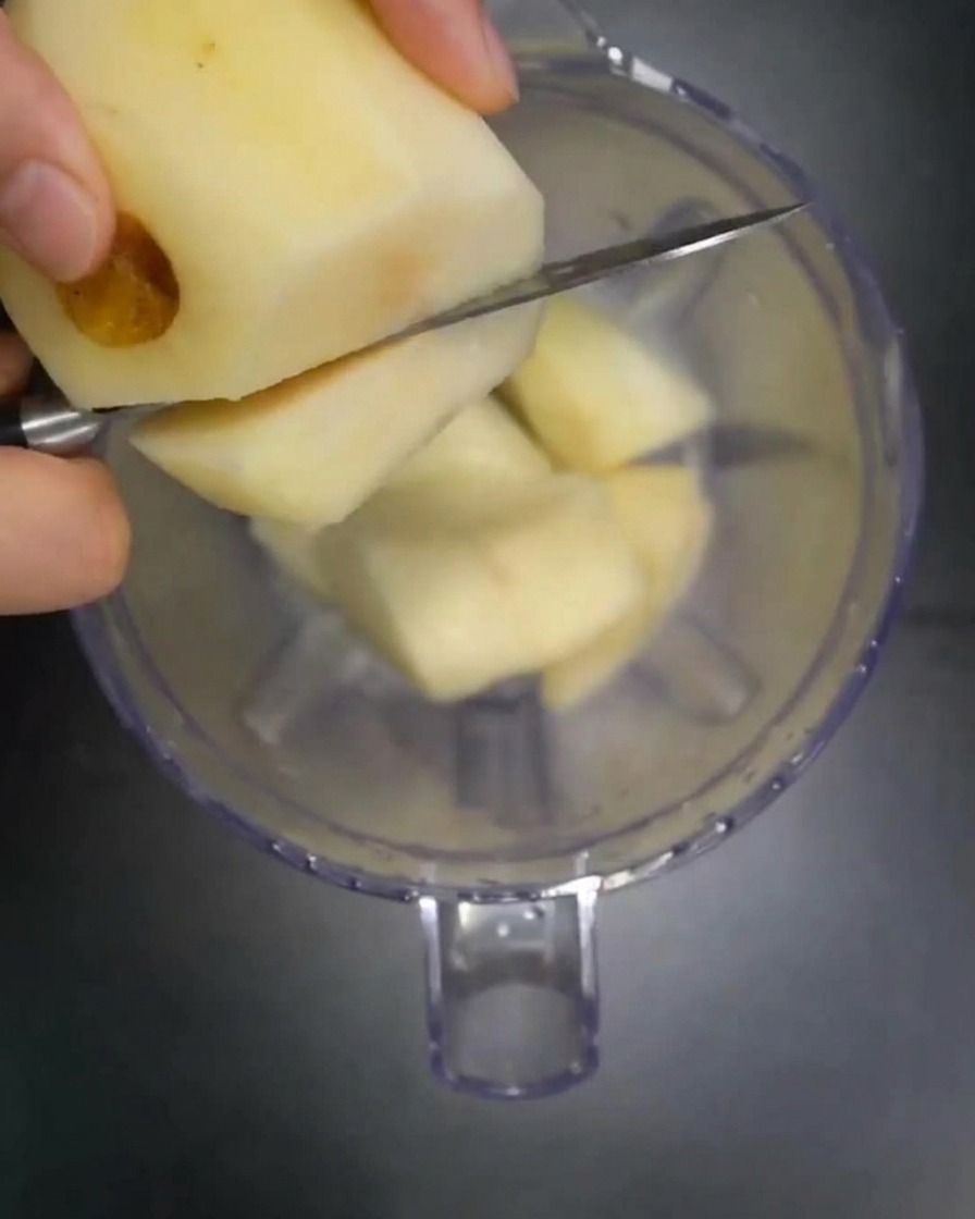 Morceaux de poire, pomme et oignon frais versés dans le bol dun mixeur.