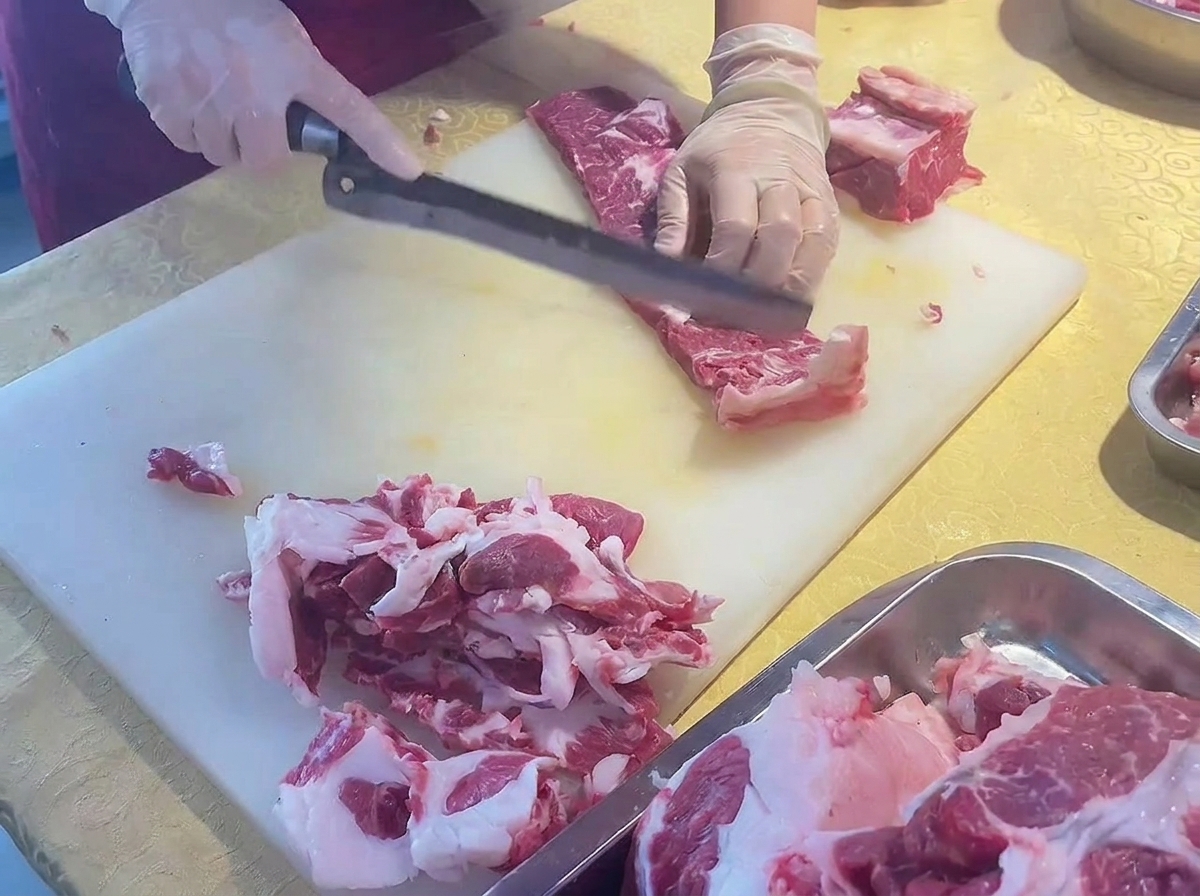Mains tranchant une côte de bœuf parée en fines lamelles à laide dun grand couteau incliné.