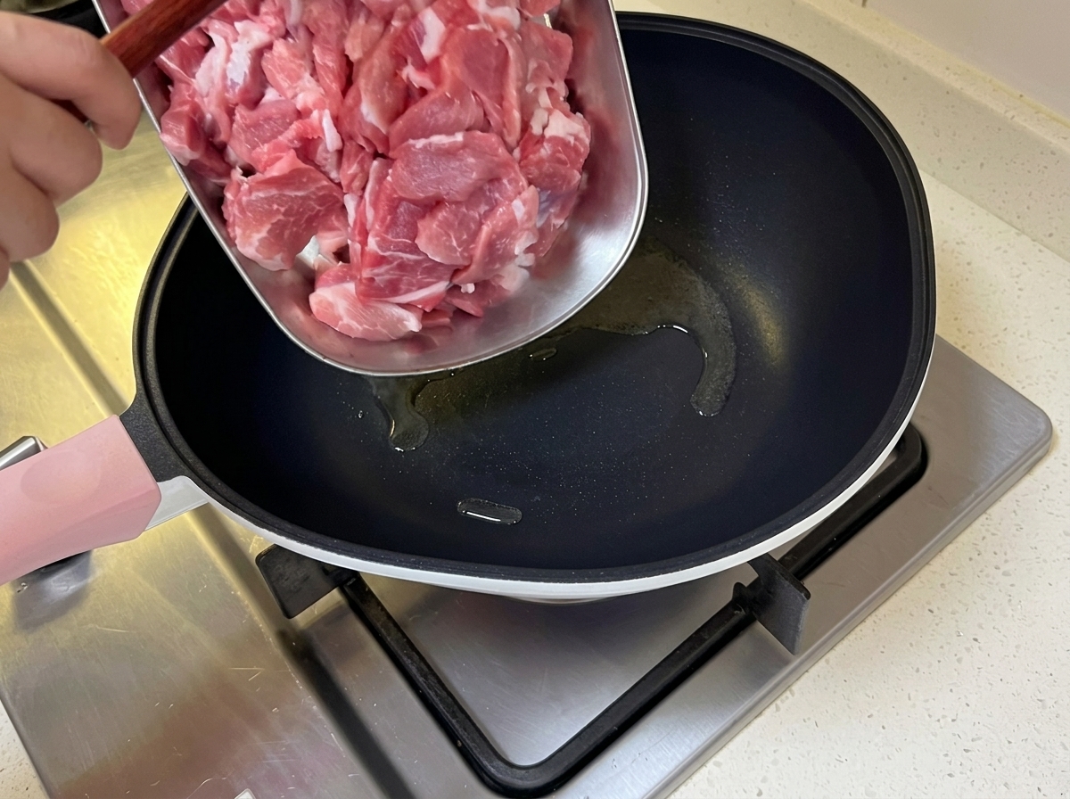 Fines tranches de porc ajoutées dans une poêle chaude contenant de lhuile frémissante.