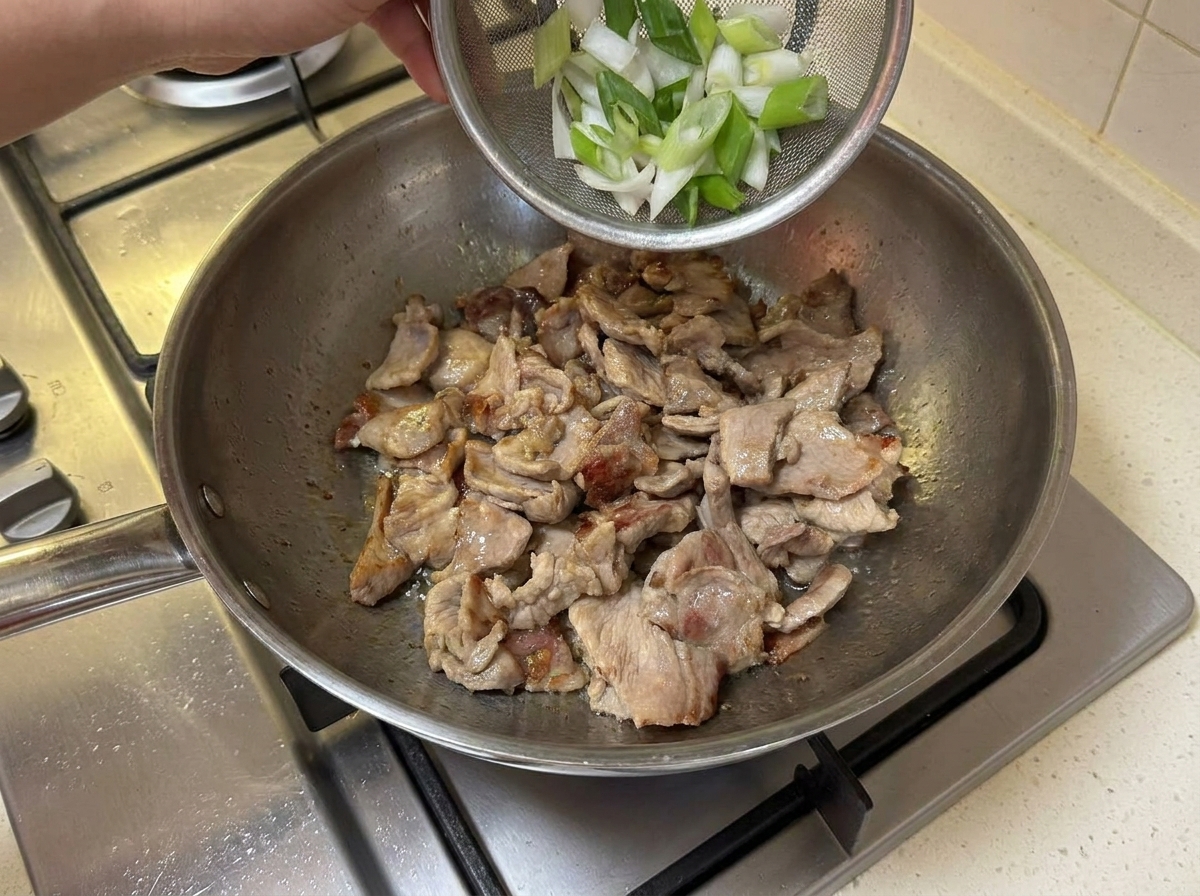 Segments doignon vert ajoutés dans la poêle avec le porc doré.