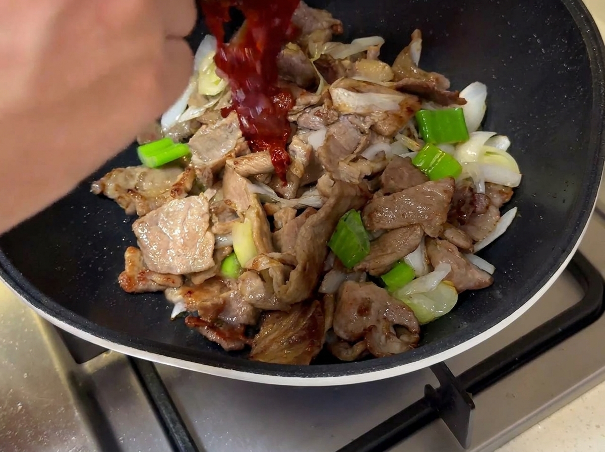 La sauce rouge versée dans la poêle sur la viande et les oignons.