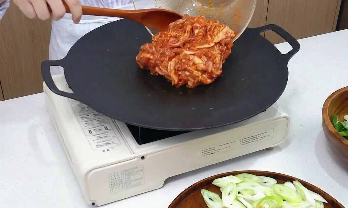 Le porc mariné épicé versé depuis un bol mélangeur dans une poêle chaude.