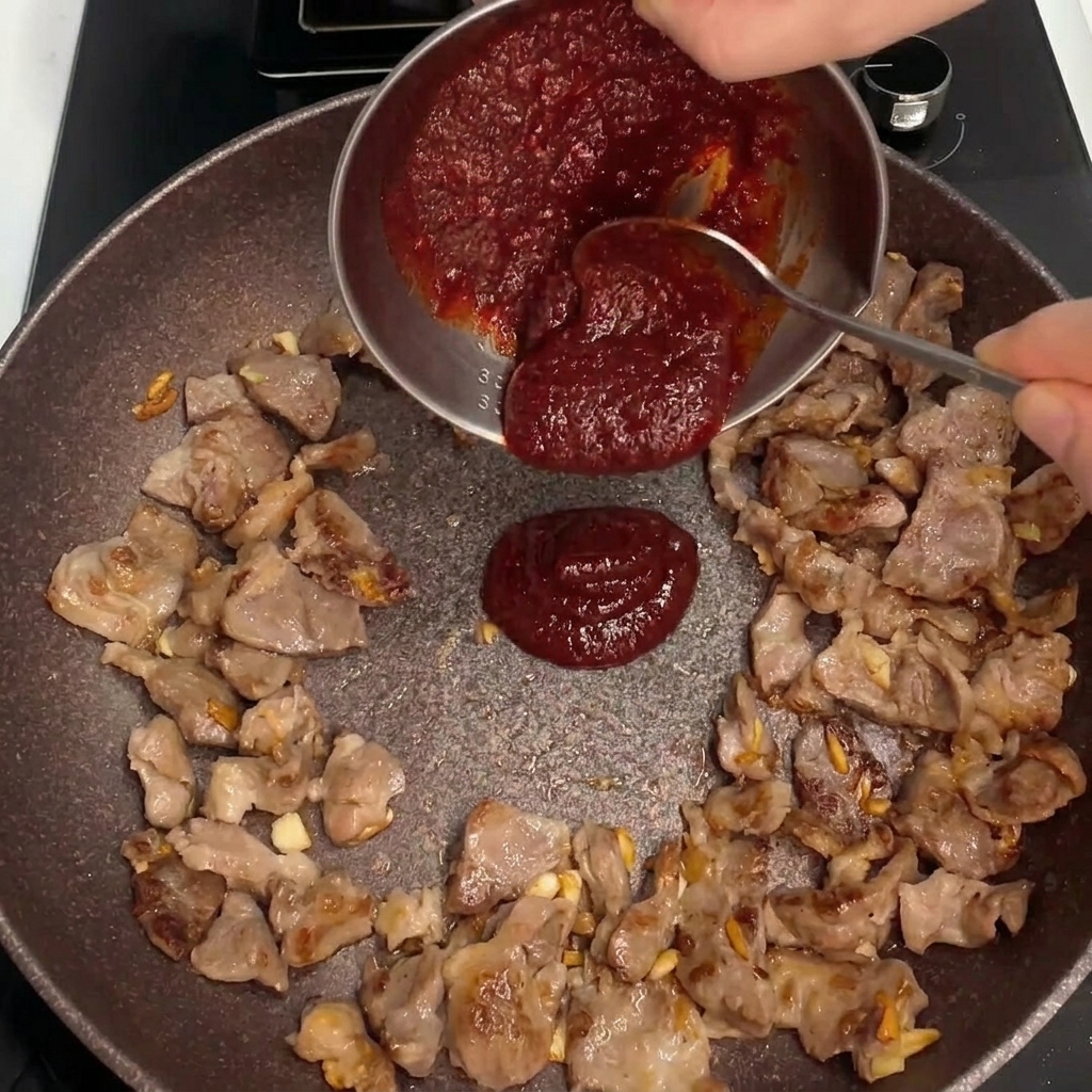 Sauce rouge épaisse versée au centre de la poêle avec le porc en train de sauter.