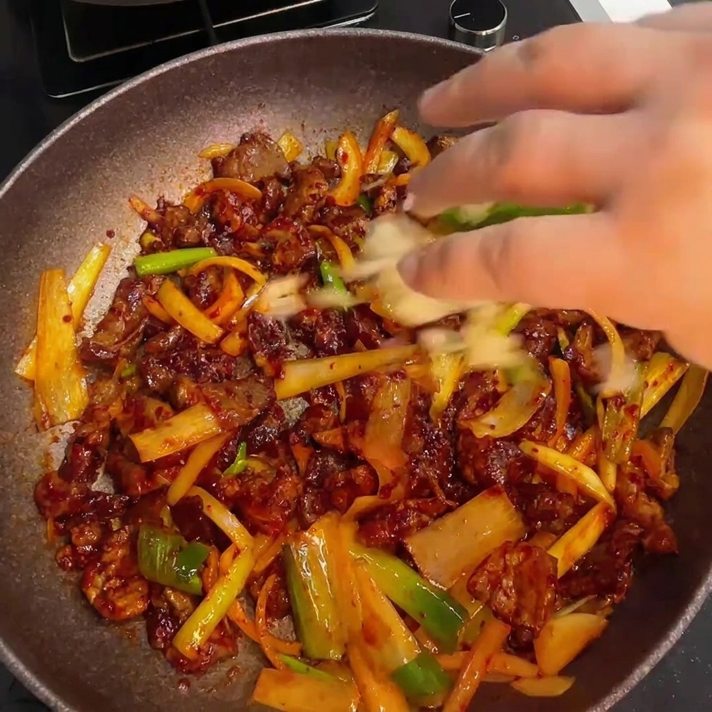 Finition du porc épicé sauté en mélangeant de lail haché frais et un filet dhuile de sésame.