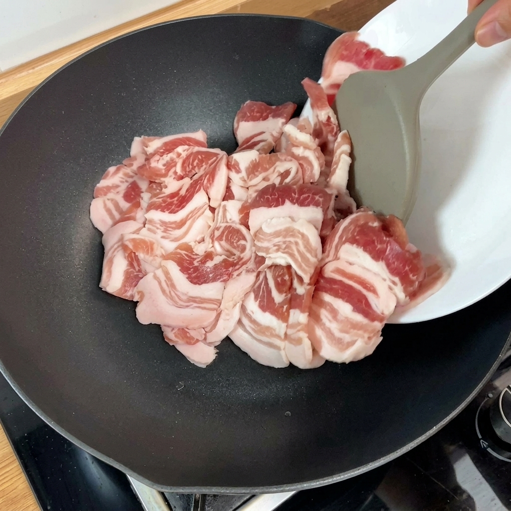 Tranches de poitrine de porc crue ajoutées dans une poêle chaude, marquant le début de la cuisson.