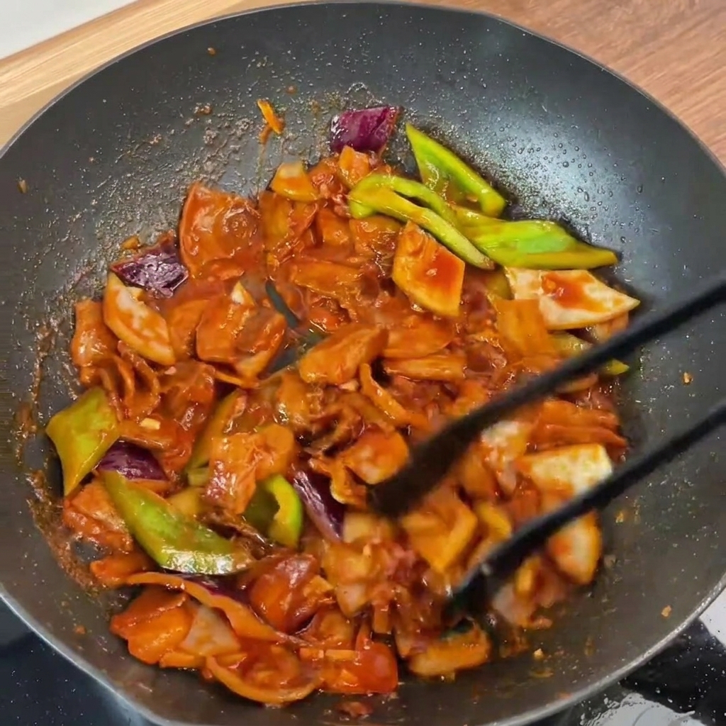 Le sauté de porc et légumes en cours de mélange dans la poêle, parfaitement enrobé de sauce brillante.