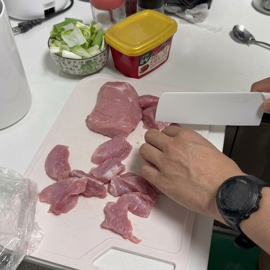 Une personne tranchant du porc cru sur une planche à découper en plastique blanc avec un couteau de cuisine blanc.