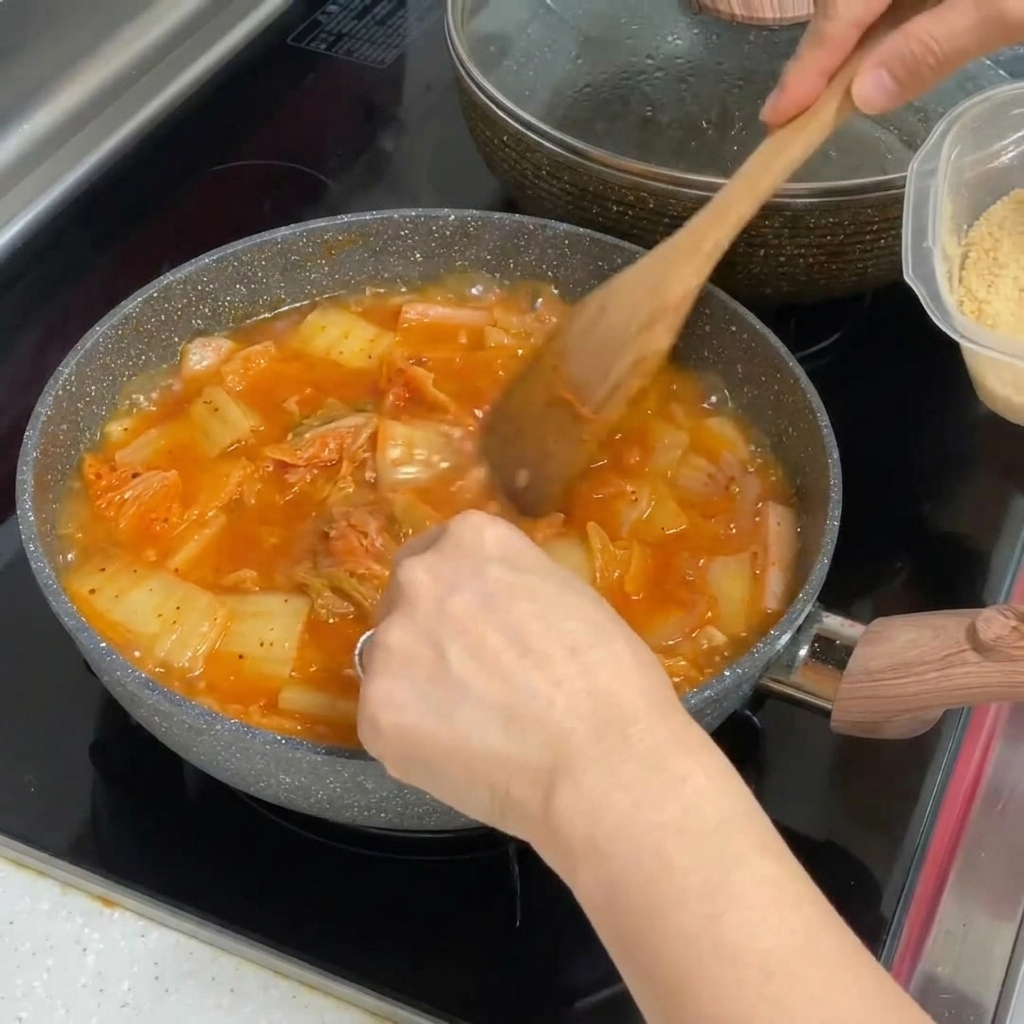 De lail émincé mélangé dans une casserole de ragoût de kimchi rouge vif.