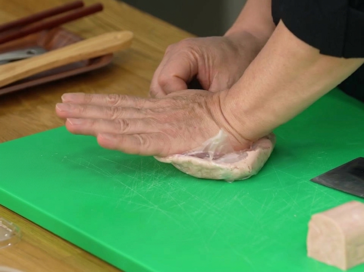 Une main pressant un sac en plastique contenant une moitié de Spam pour lécraser en pâte.