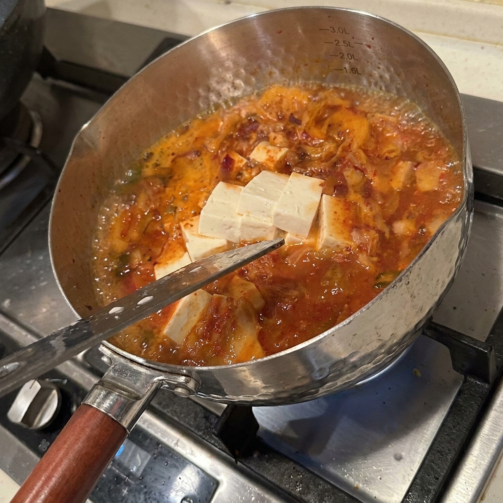 Tofu, champignons, poivrons et kimchi mijotant dans le bouillon rouge.