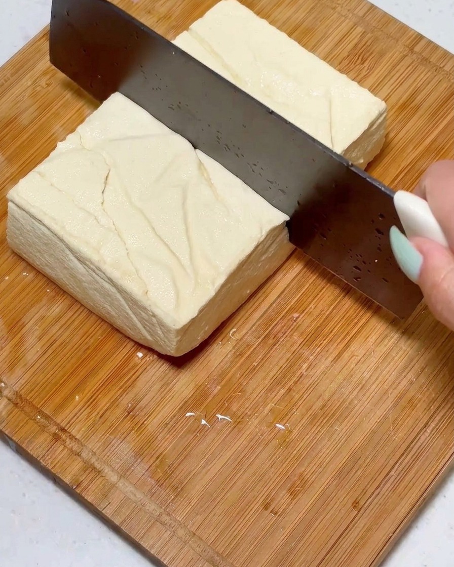 Découpe dun bloc de tofu ferme en morceaux uniformes à laide dun grand couteau sur une surface en bois.