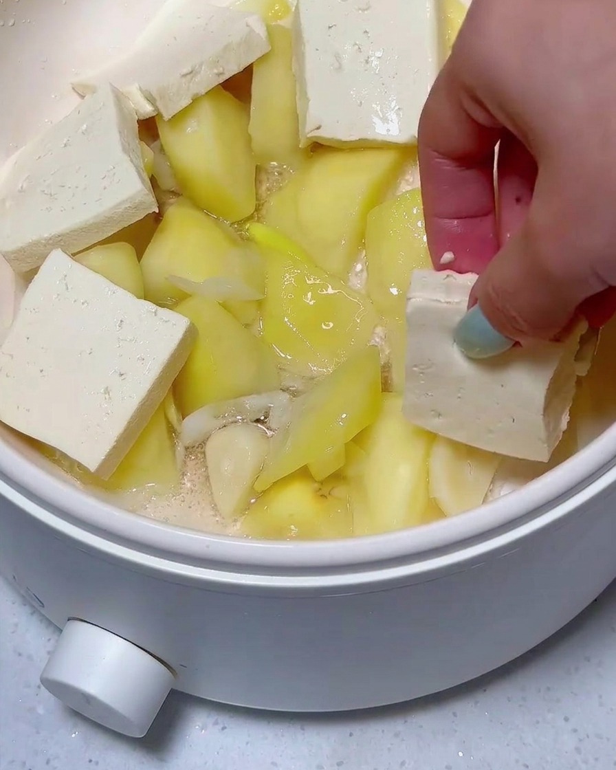 Tranches de tofu et de jambon disposées soigneusement sur un lit de pommes de terre dans la poêle.