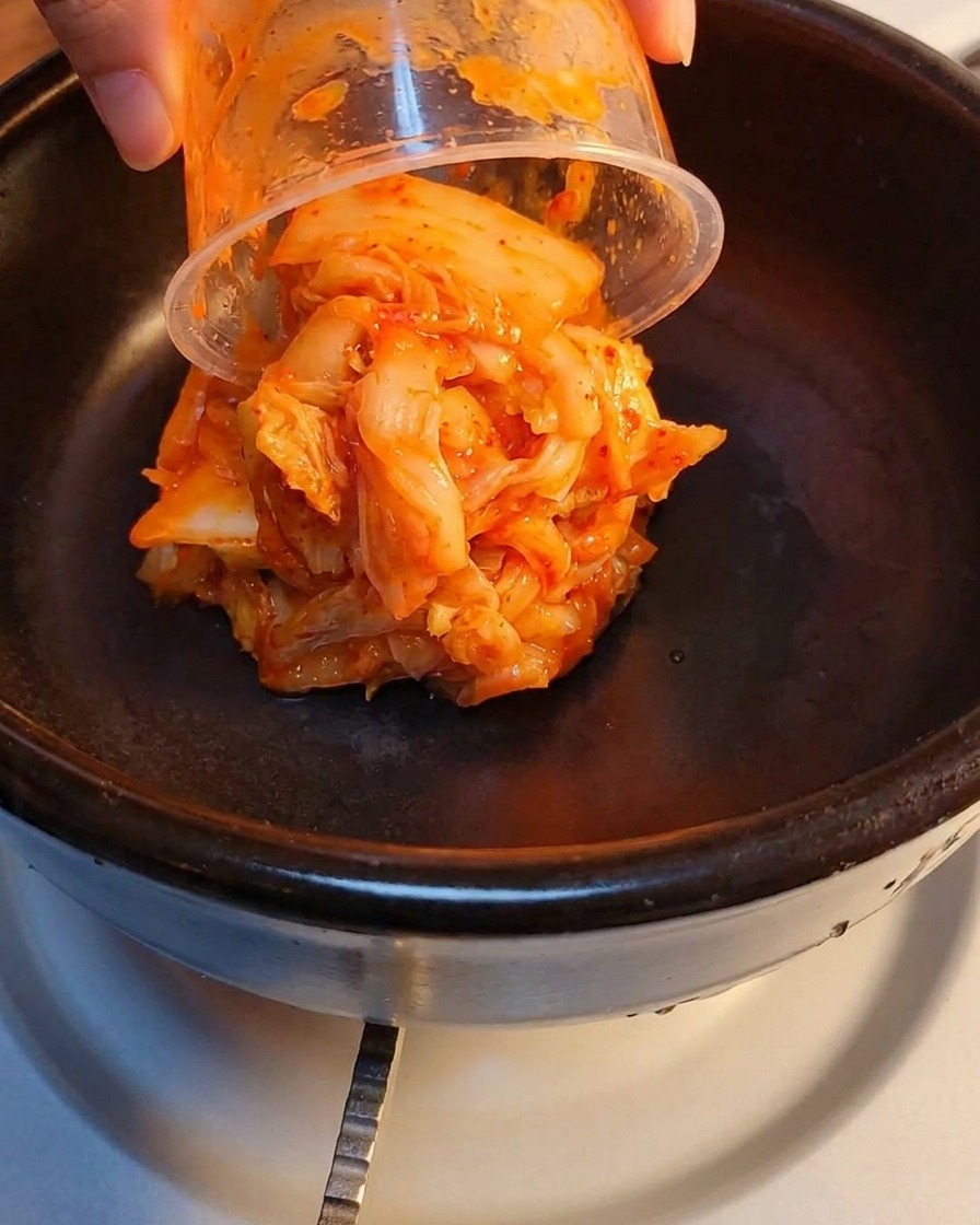Kimchi fermenté et jambon écrasé superposés dans un pot en pierre.