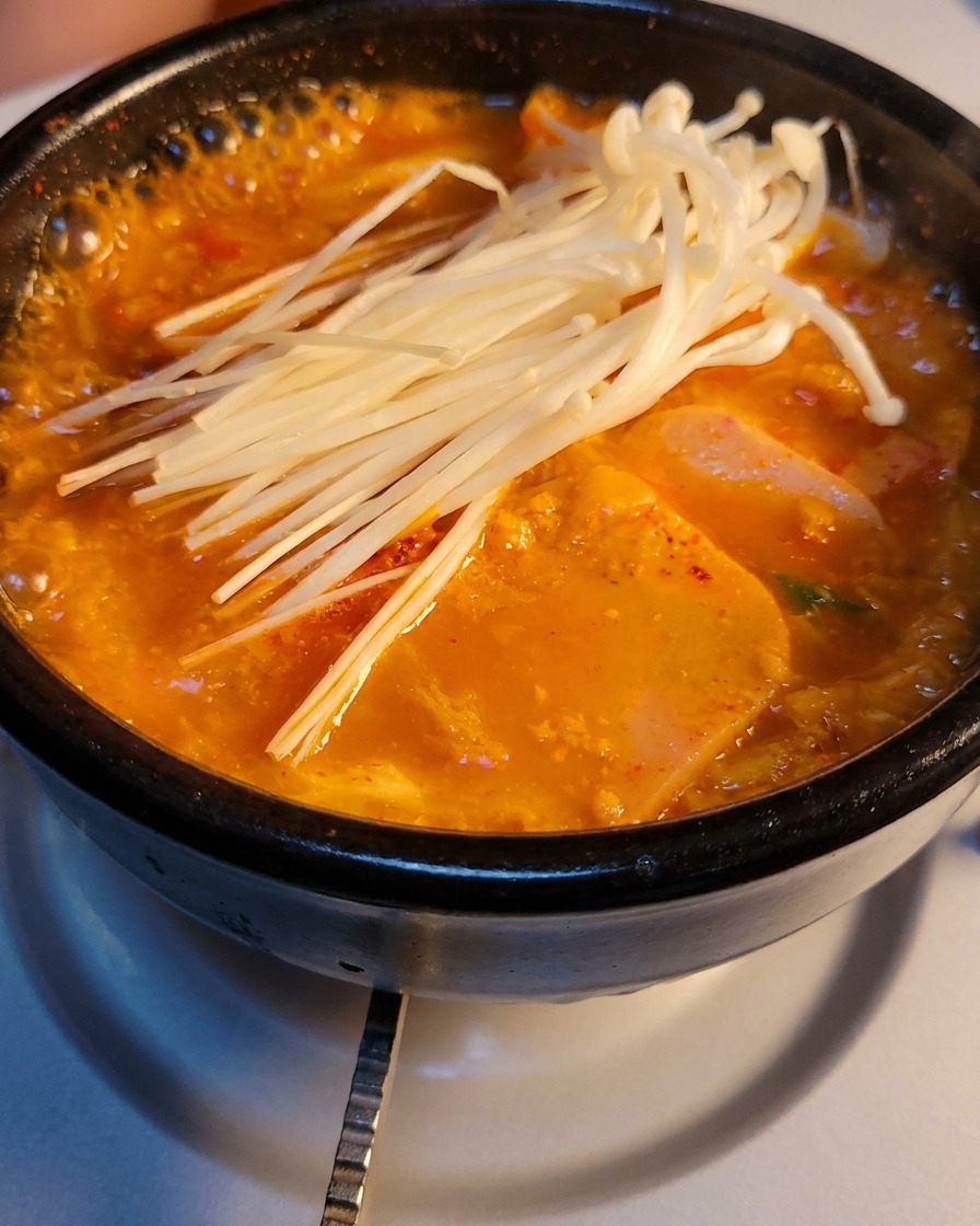 Un pot en pierre de soupe au kimchi bouillonnante garni de champignons enoki frais.
