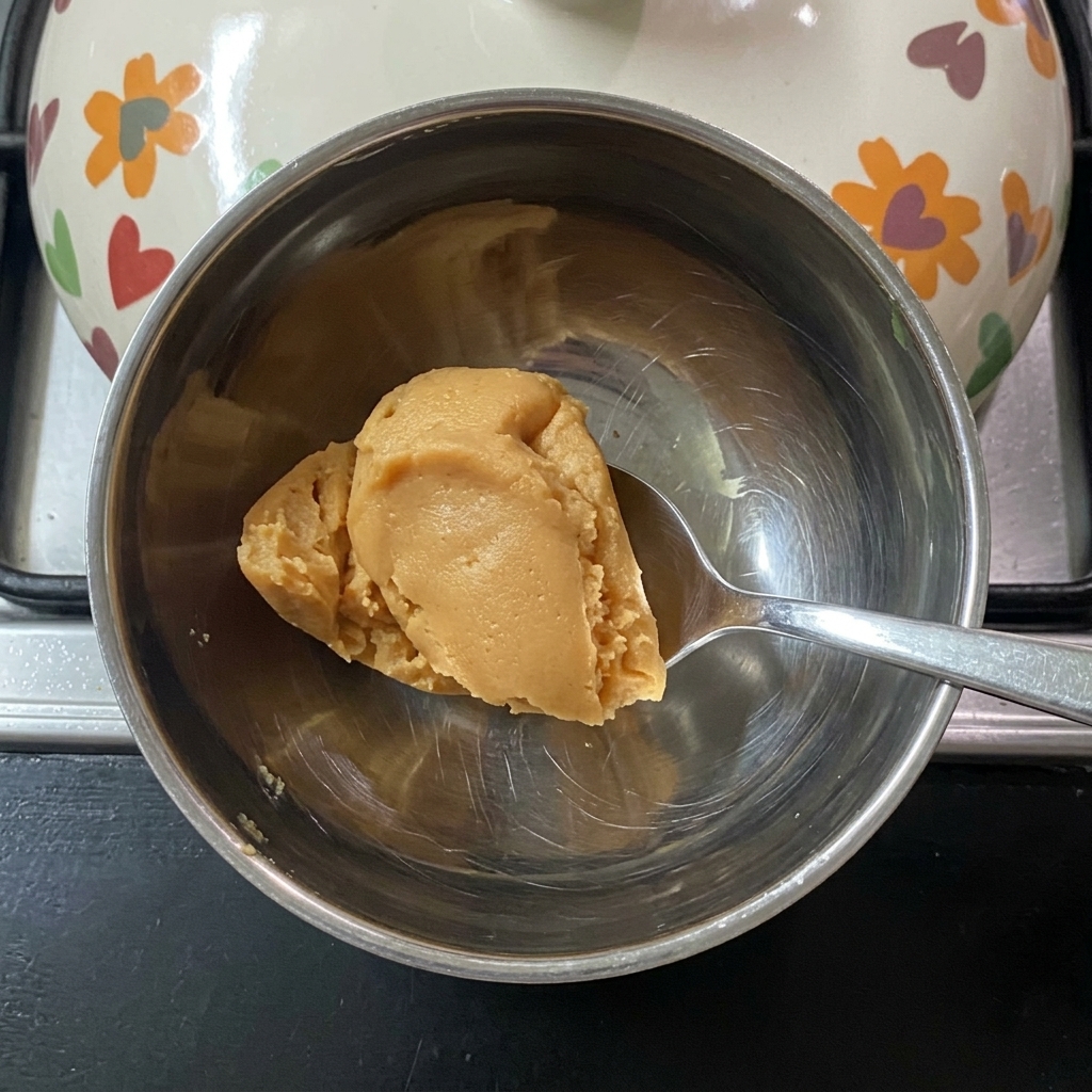 Une cuillère mélangeant la pâte de miso dans de leau tiède dans un petit bol.