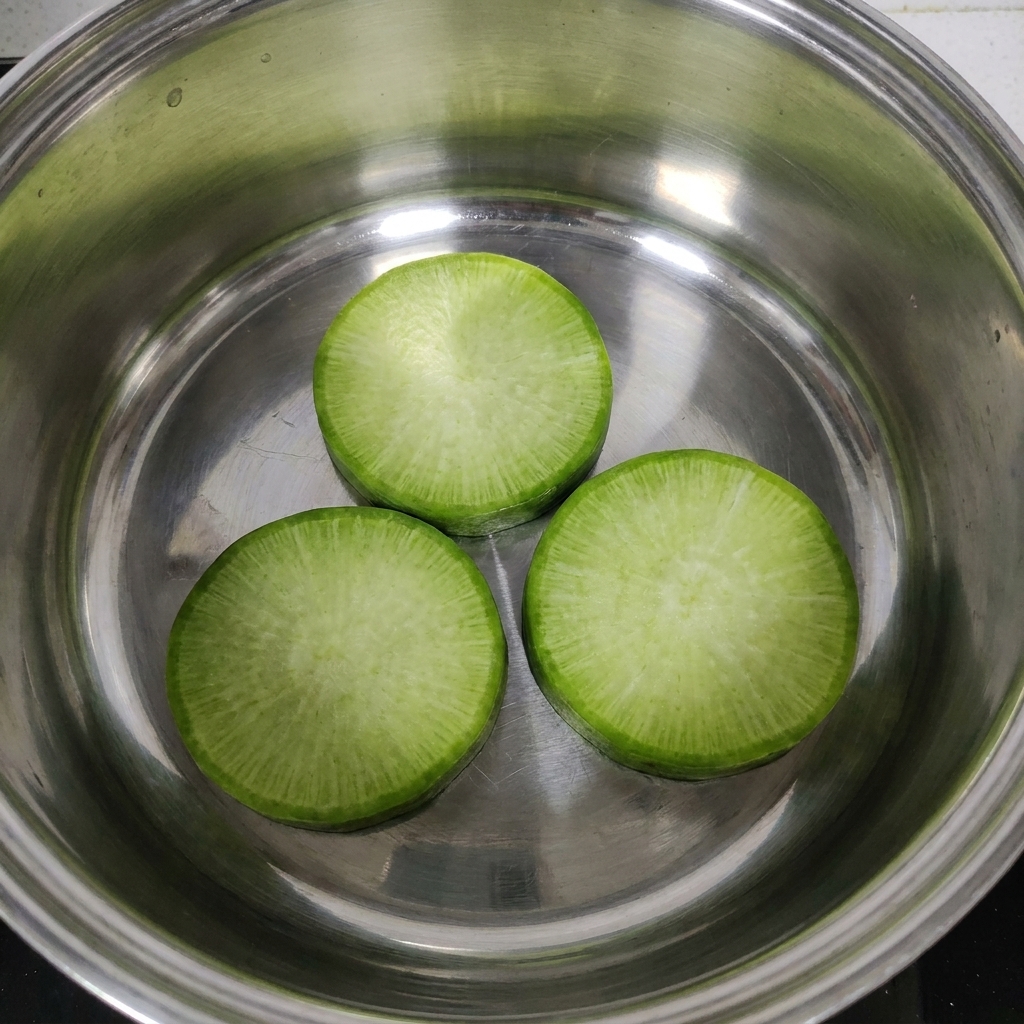 Tranches de radis disposées au fond dune casserole en inox.