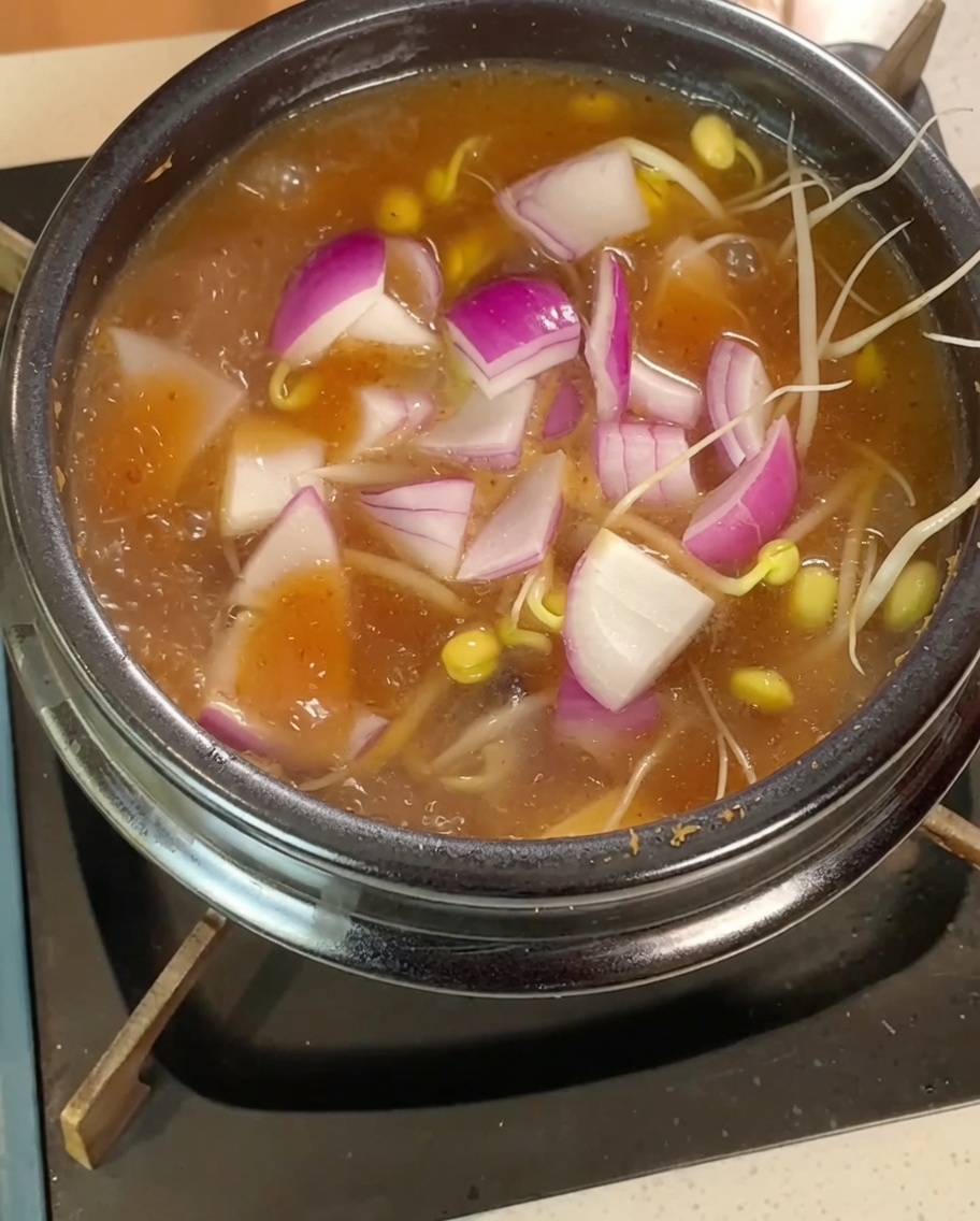 Des pousses de soja, des tranches doignon rouge et du tofu en dés mijotant dans le bouillon bouillonnant.