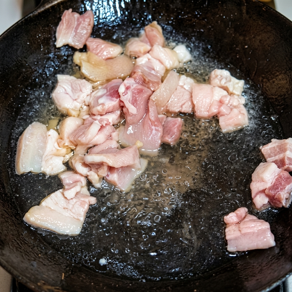 Morceaux de poitrine de porc dorant dans du saindoux fondu dans un wok traditionnel.