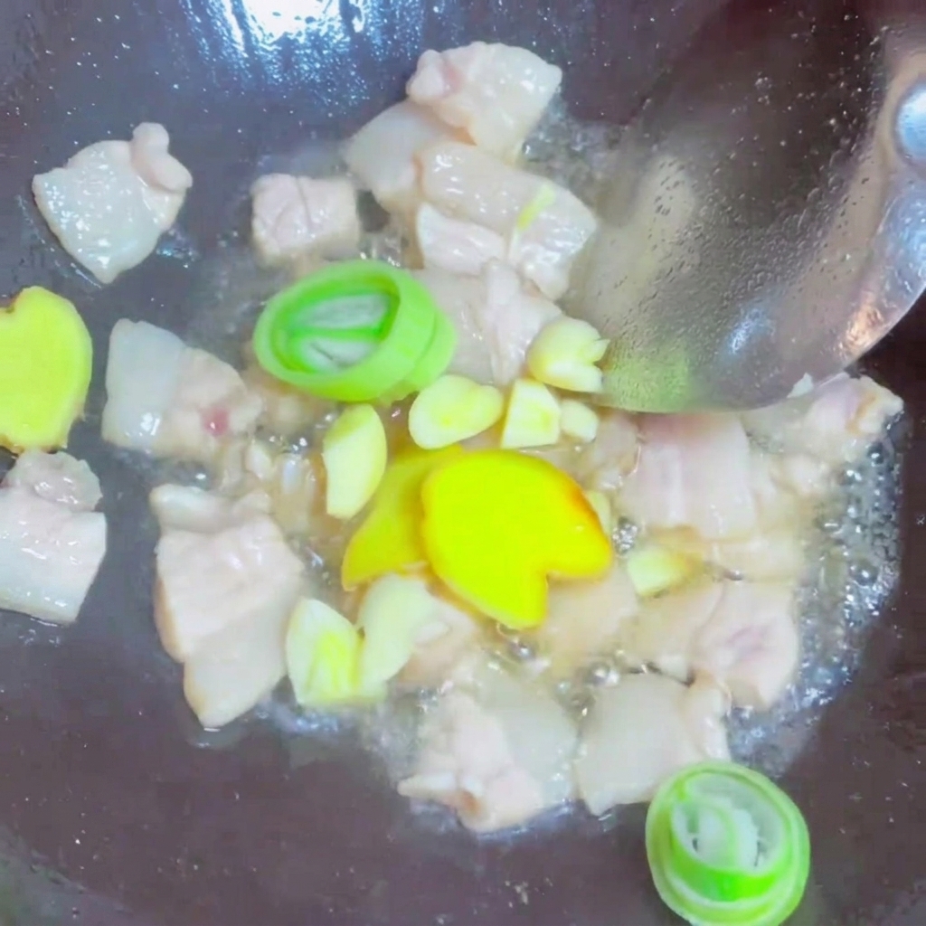 Tranches de gingembre frais, ail et anneaux doignon vert sautés avec des morceaux de porc dans un wok.
