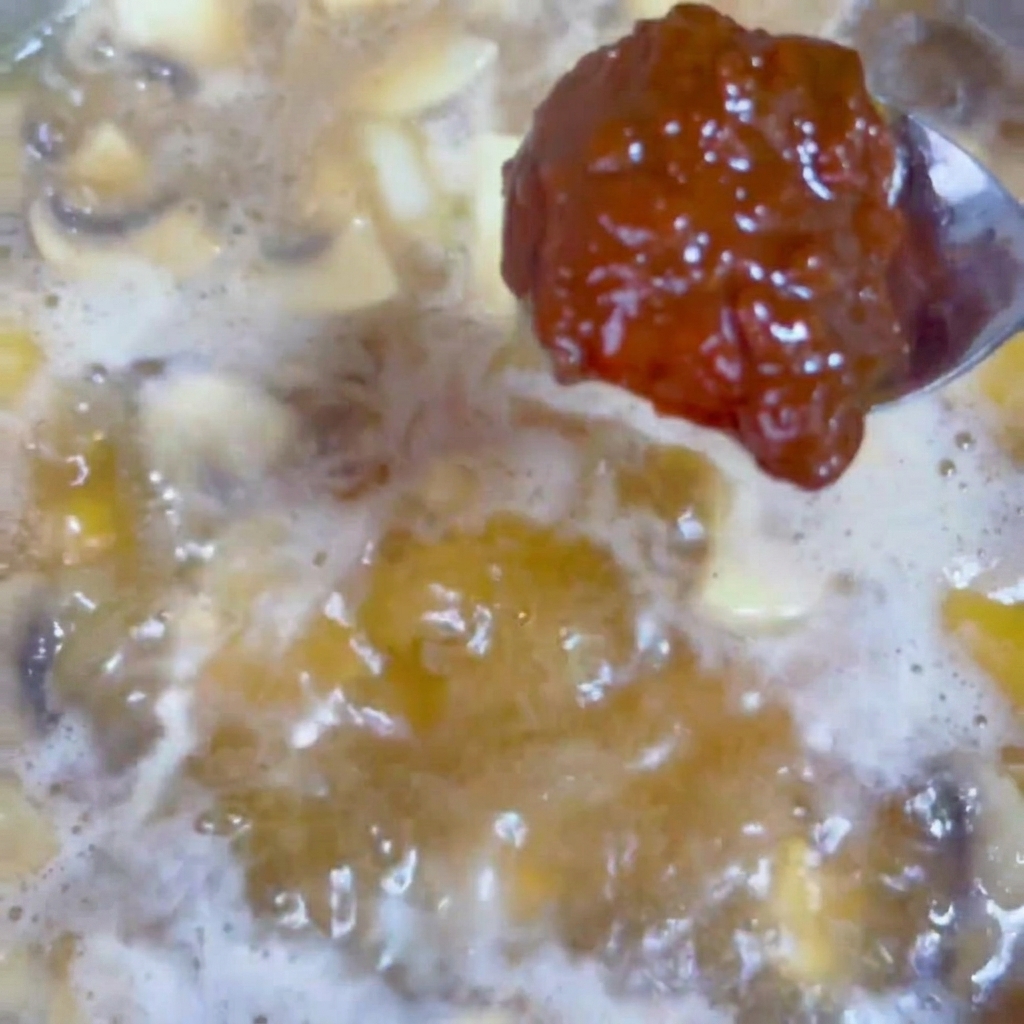 Une cuillerée de pâte de soja riche et sombre incorporée dans un bouillon savoureux bouillonnant dans un wok.