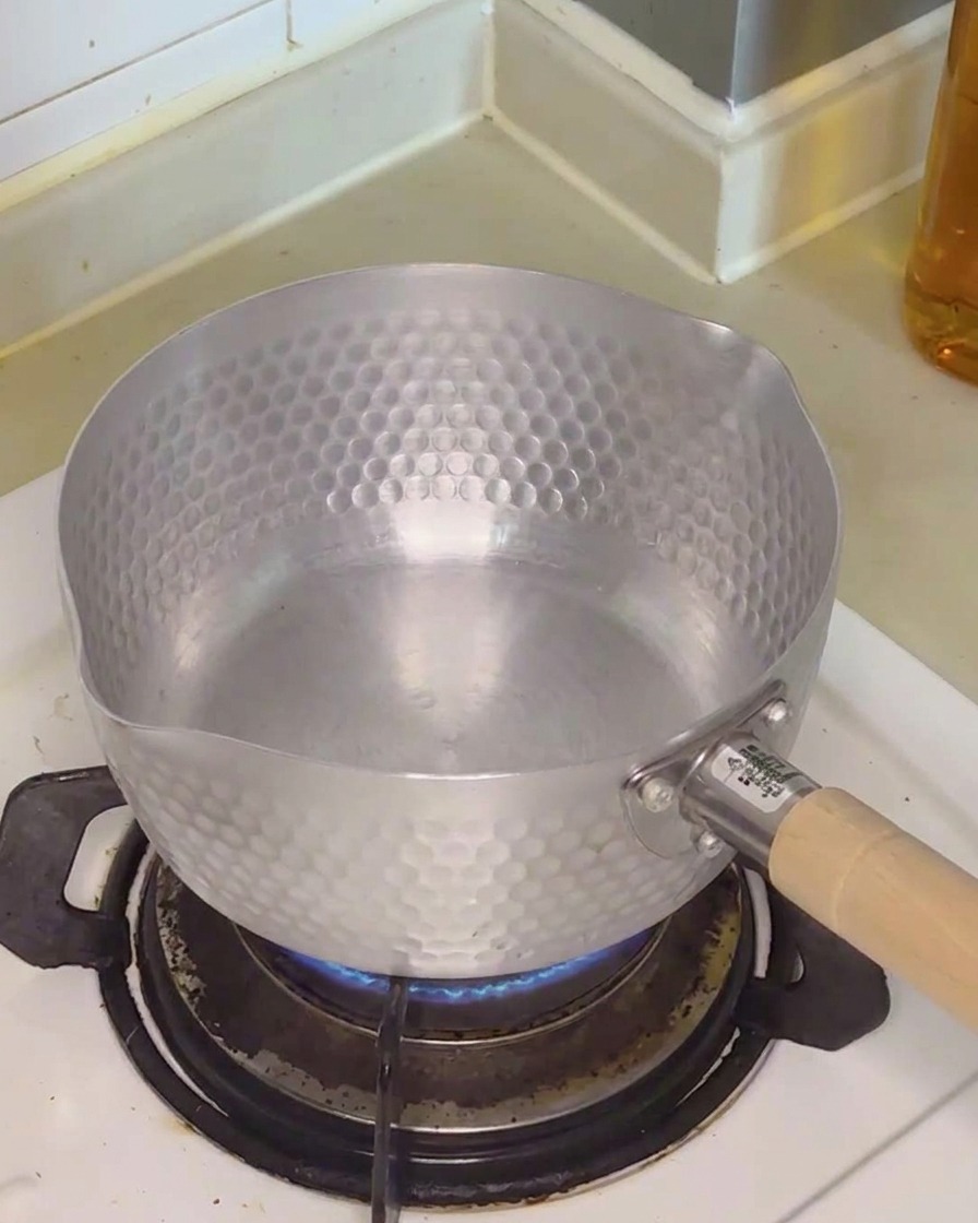 Eau claire versée dans une petite casserole en métal sur une plaque de cuisson.