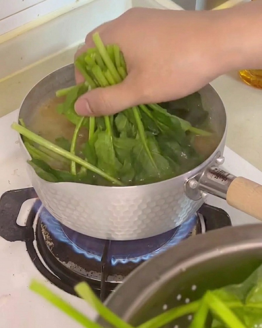 Épinards, cubes de tofu et champignons enoki incorporés dans la soupe bouillante.
