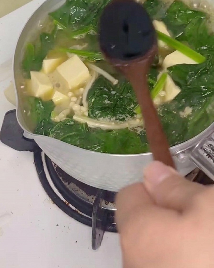 Sauce soja versée dans la soupe fumante et mélangée avec une cuillère en bois.