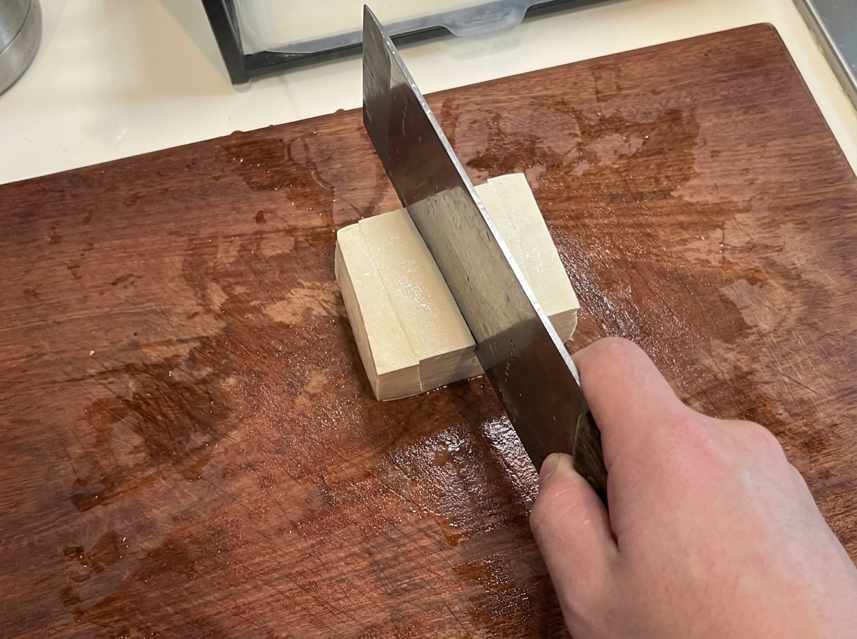 Un bloc de tofu ferme coupé en cubes réguliers sur une planche.