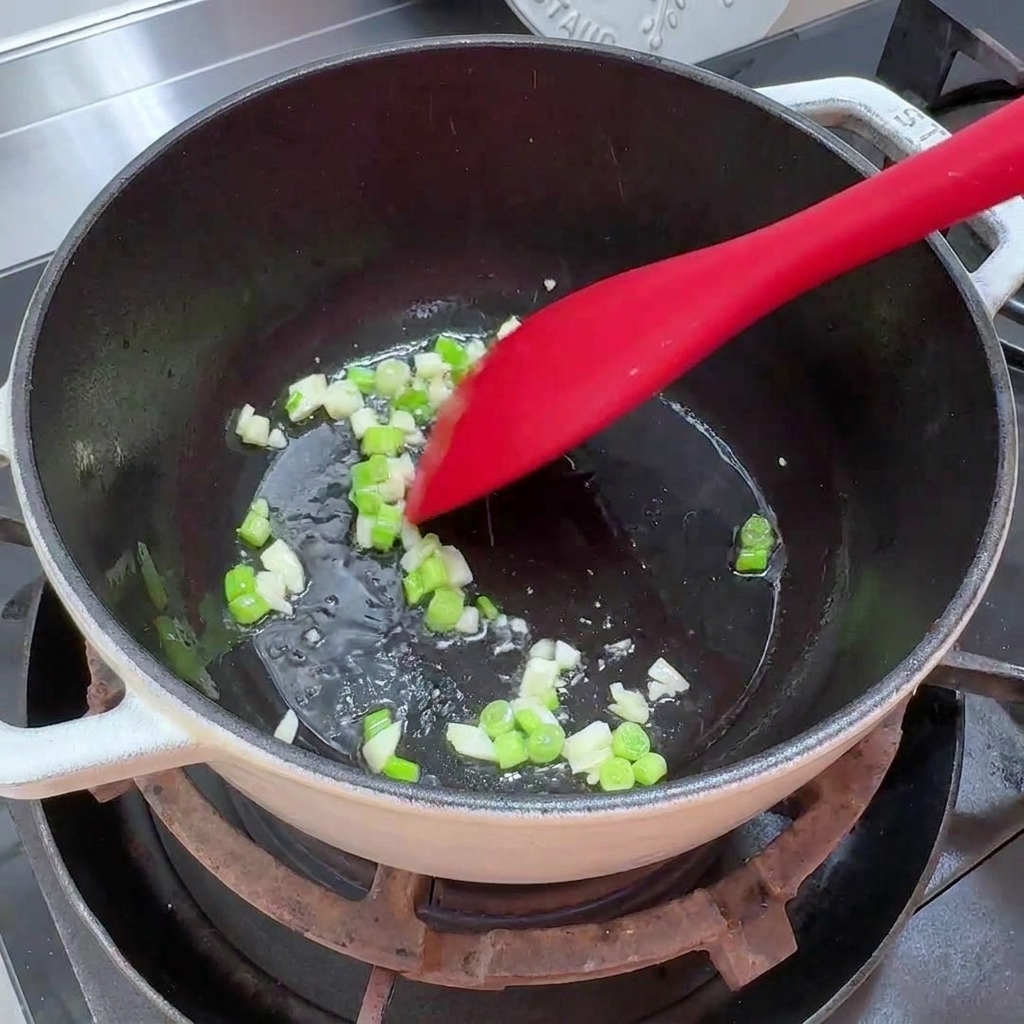 Oignons verts hachés et ail émincé en train de revenir dans une casserole avec un peu dhuile.