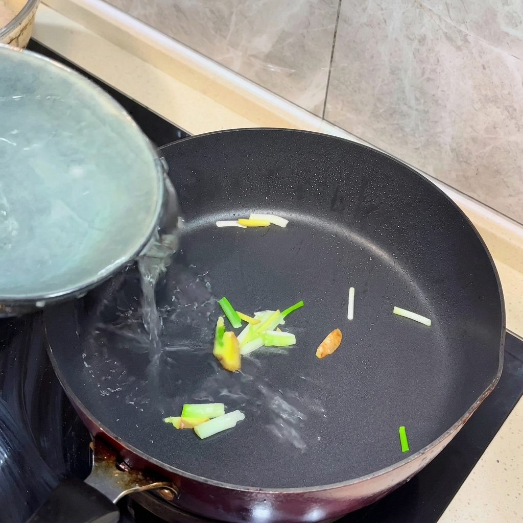 Eau bouillante versée dans une casserole avec du gingembre et des oignons verts sautés.