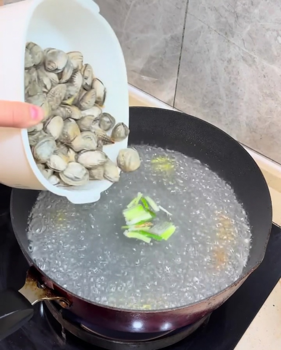 Des palourdes fraîches et des cubes de tofu sont ajoutés au bouillon en ébullition.
