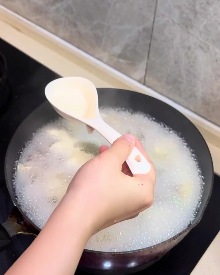 Une cuillère écumant la mousse blanche à la surface de la soupe frémissante aux palourdes et au tofu.