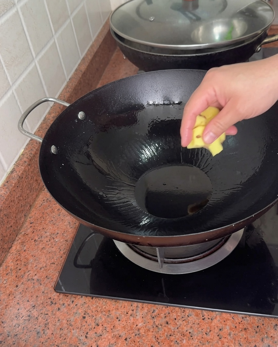 Une main ajoutant un morceau de gingembre dans un wok chaud avec de lhuile.
