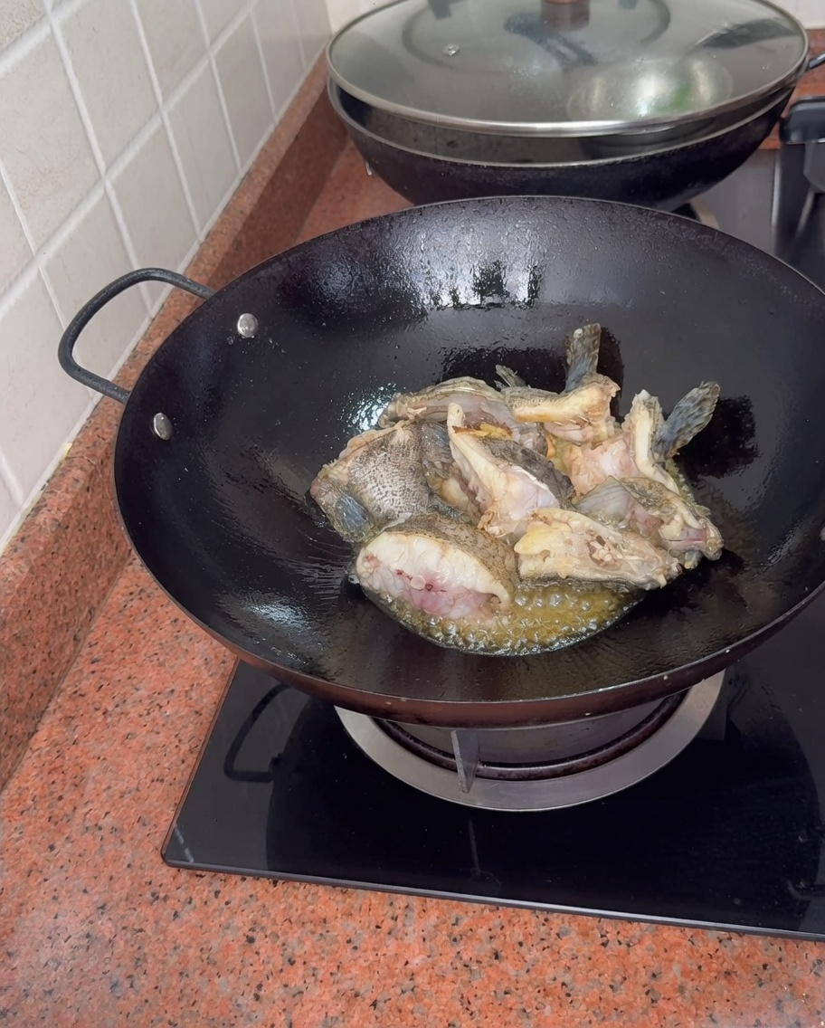 Morceaux de mérou mijotant dans un wok pendant que de leau bouillante est ajoutée, créant un fond de poisson blanc épais.