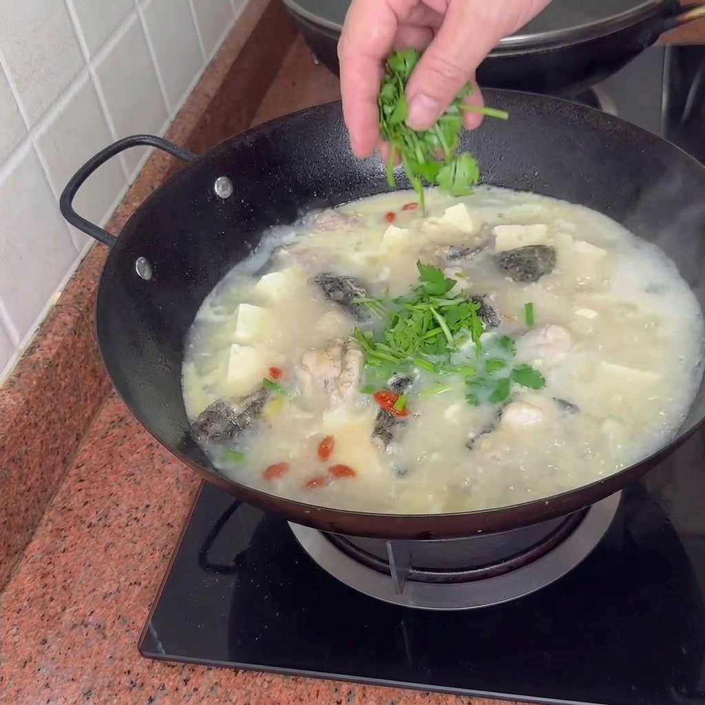Une marmite terminée de soupe crémeuse au poisson, tofu et palourdes garnie doignons verts vibrants.