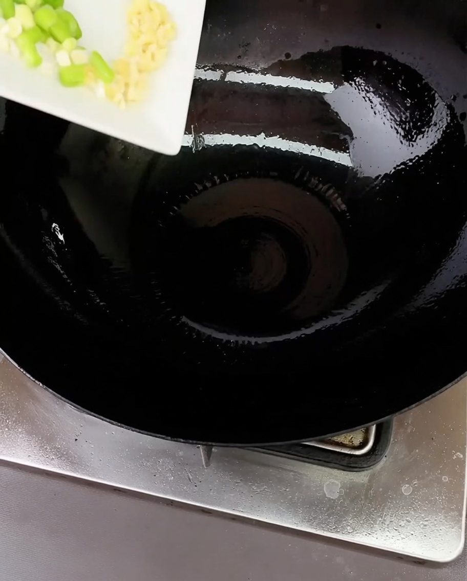 Oignons verts hachés et ail émincé en train de grésiller dans un wok huilé.