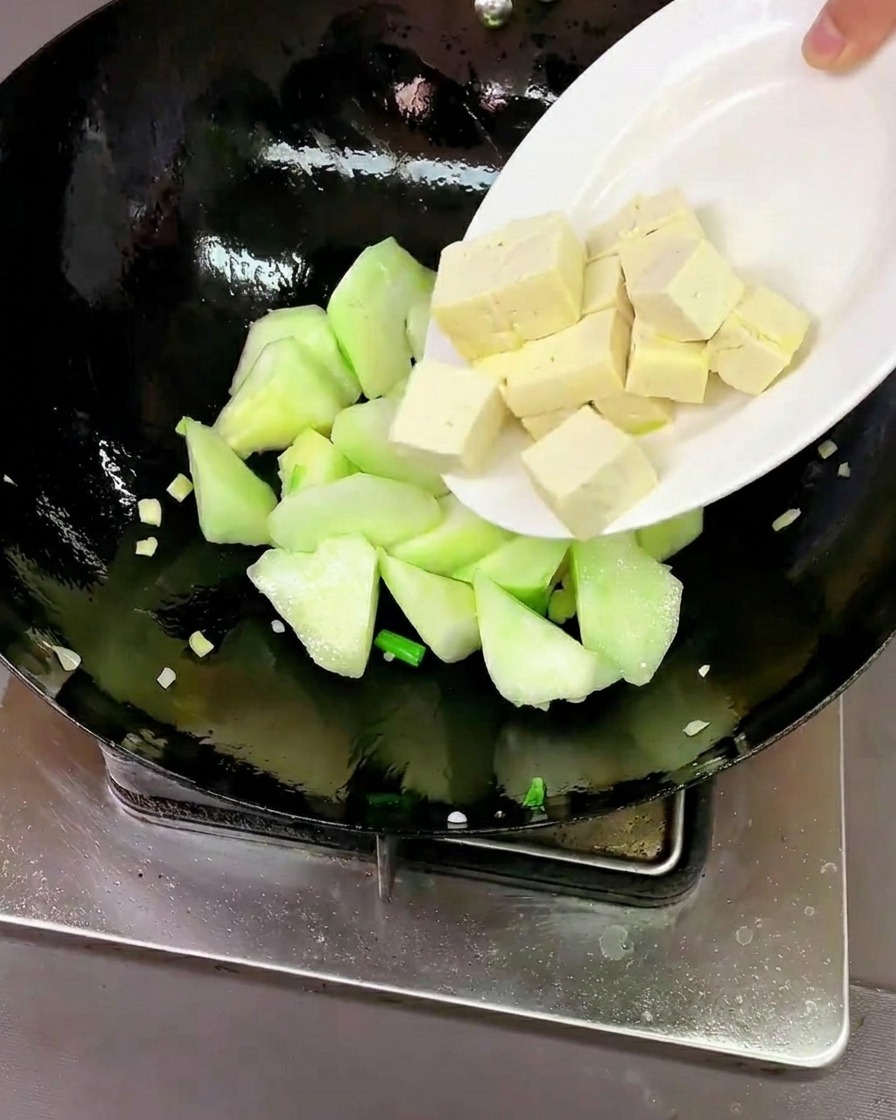 Cubes de tofu et palourdes crues ajoutés au wok avec le luffa.
