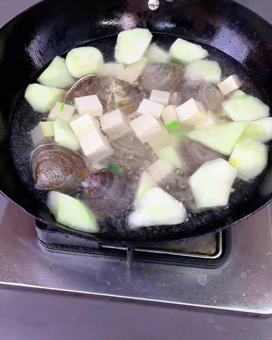 Eau versée sur le mélange dans le wok, prêt à être couvert.