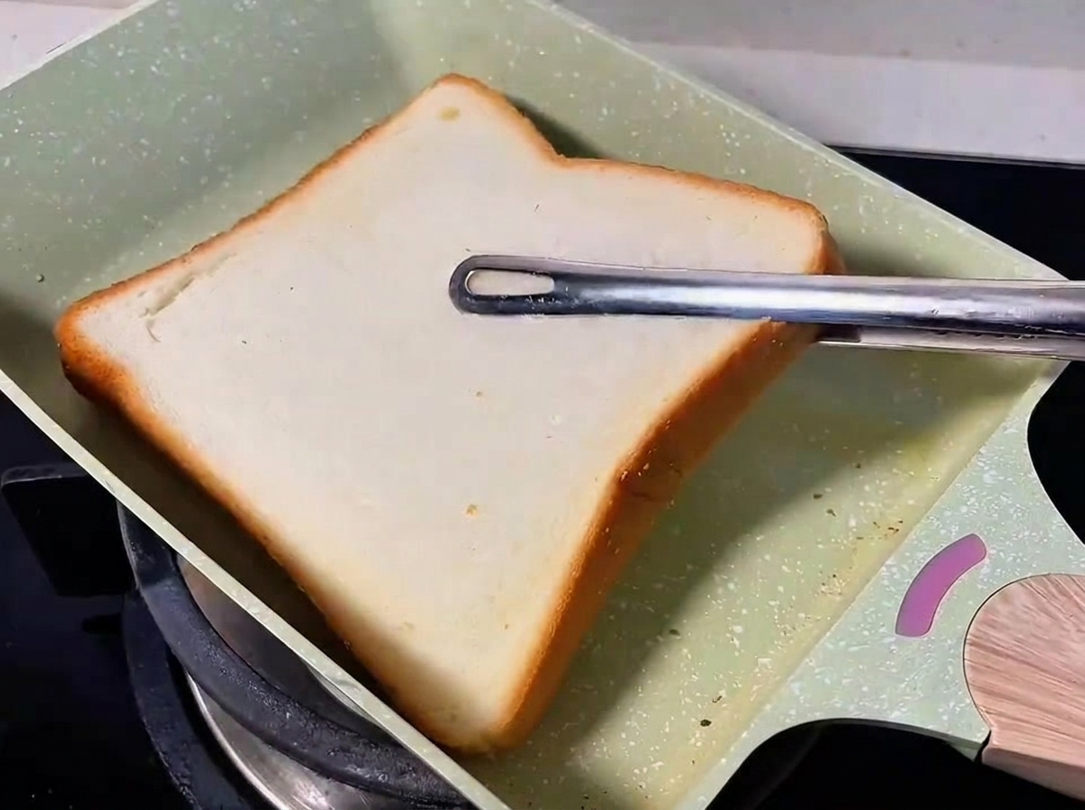 Une tranche de pain blanc grillant dans une poêle verte.