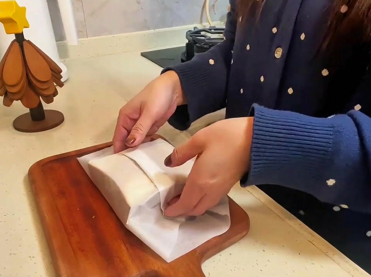 Le sandwich fini emballé dans du papier sulfurisé en cours de découpe sur une planche en bois.