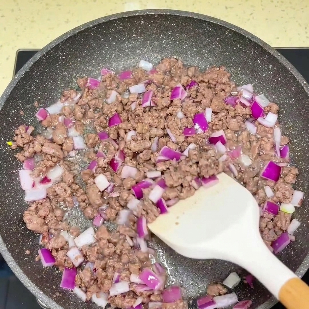Bœuf haché sauté et oignon rouge haché assaisonnés avec des sauces dans une poêle.