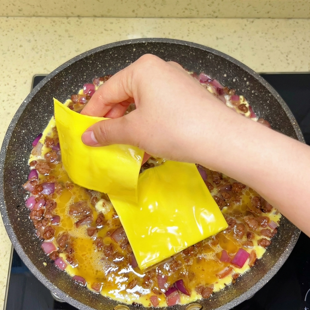 Tranches de fromage fondu déposées sur les œufs et le bœuf dans une poêle.