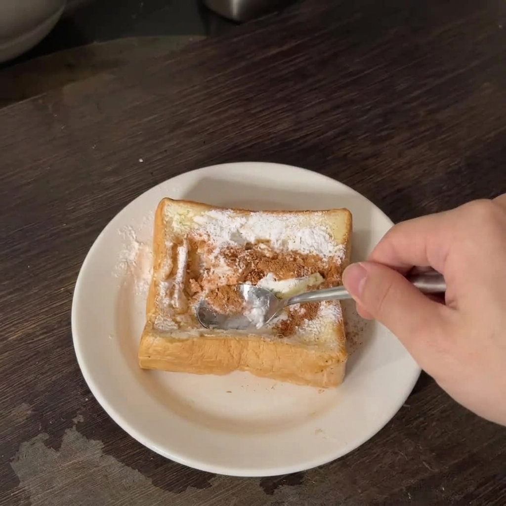 Une main utilisant une cuillère en métal pour presser le centre dune tranche de pain épais sur une assiette blanche.