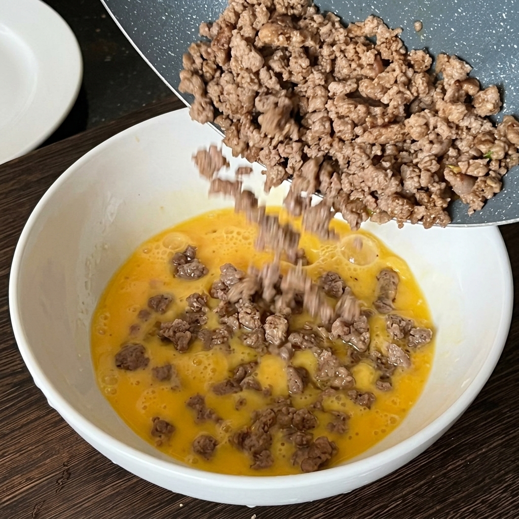 Bœuf haché cuit versé dune poêle dans un bol dœufs battus crus.
