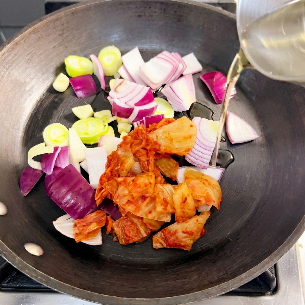 Une poêle contenant des oignons rouges, des oignons verts et du kimchi en train de revenir dans de lhuile.