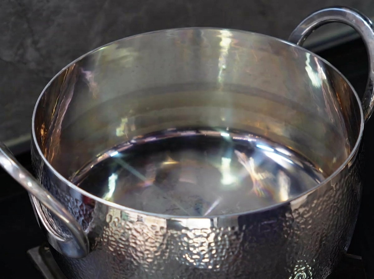 Gros plan sur une cuillère dhuile de cuisson versée dans une marmite en acier inoxydable vide et brillante.