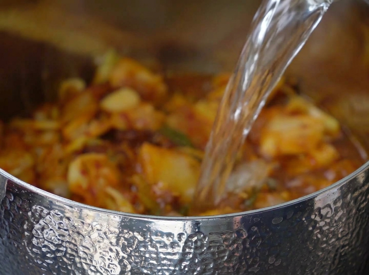 Eau versée dans la marmite contenant le mélange de kimchi et de porc.
