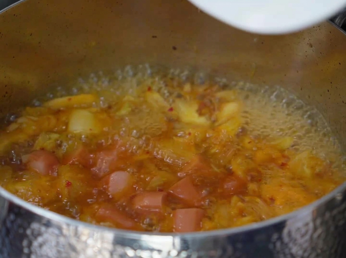 Tranches de spam et de saucisse mijotant dans le bouillon de kimchi bouillonnant.