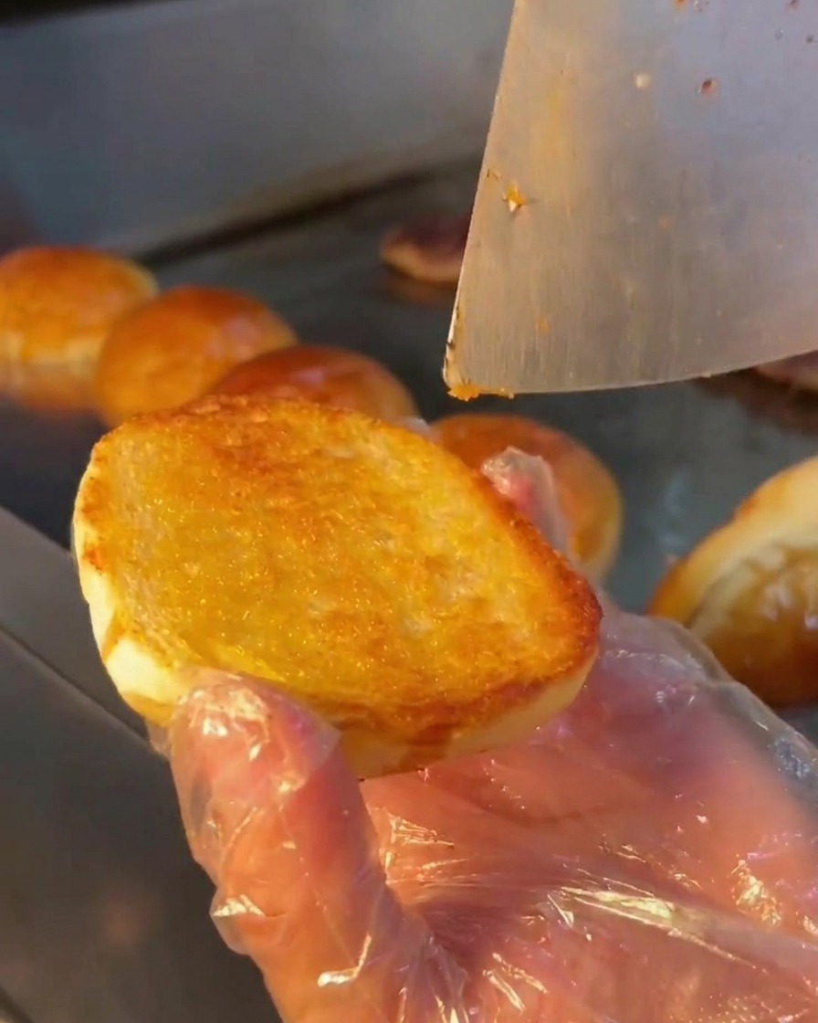 Une cuillère en métal étalant une sauce crémeuse sur la surface grillée dun pain burger.